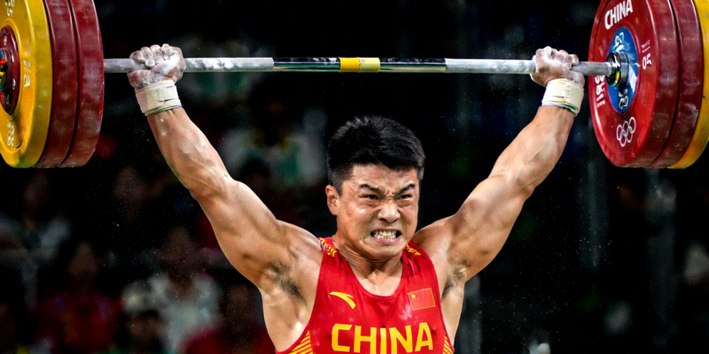 中国举重运动员在赛场上奋力举起杠铃，表情坚毅的特写镜头